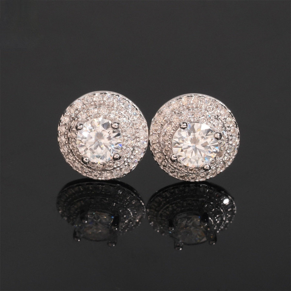 Pair of round halo stud earrings with clear center and surrounding stones on a dark surface