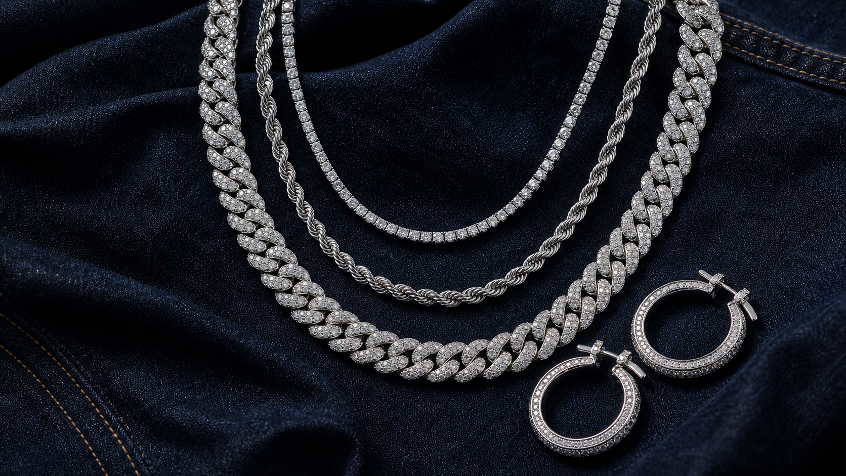 Layered silver-tone chains and hoop earrings arranged on dark denim