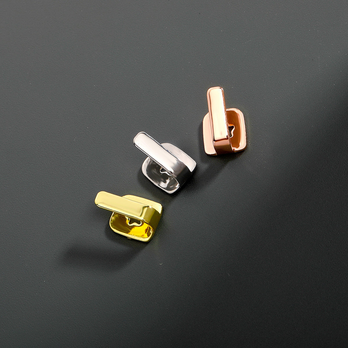 Gold, Silver and Rose Gold bar tooth caps on a gray surface