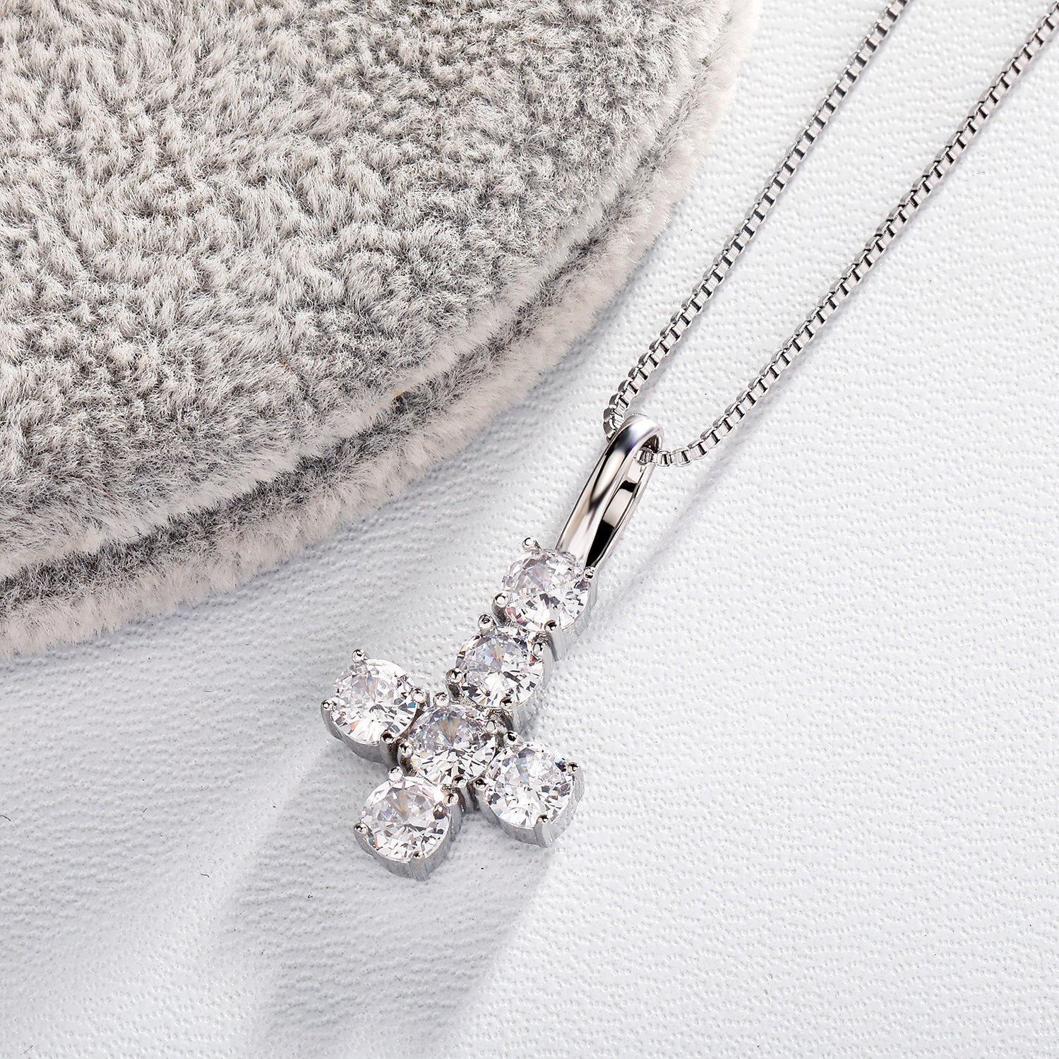 Silver iced inverted cross pendant on white textured fabric