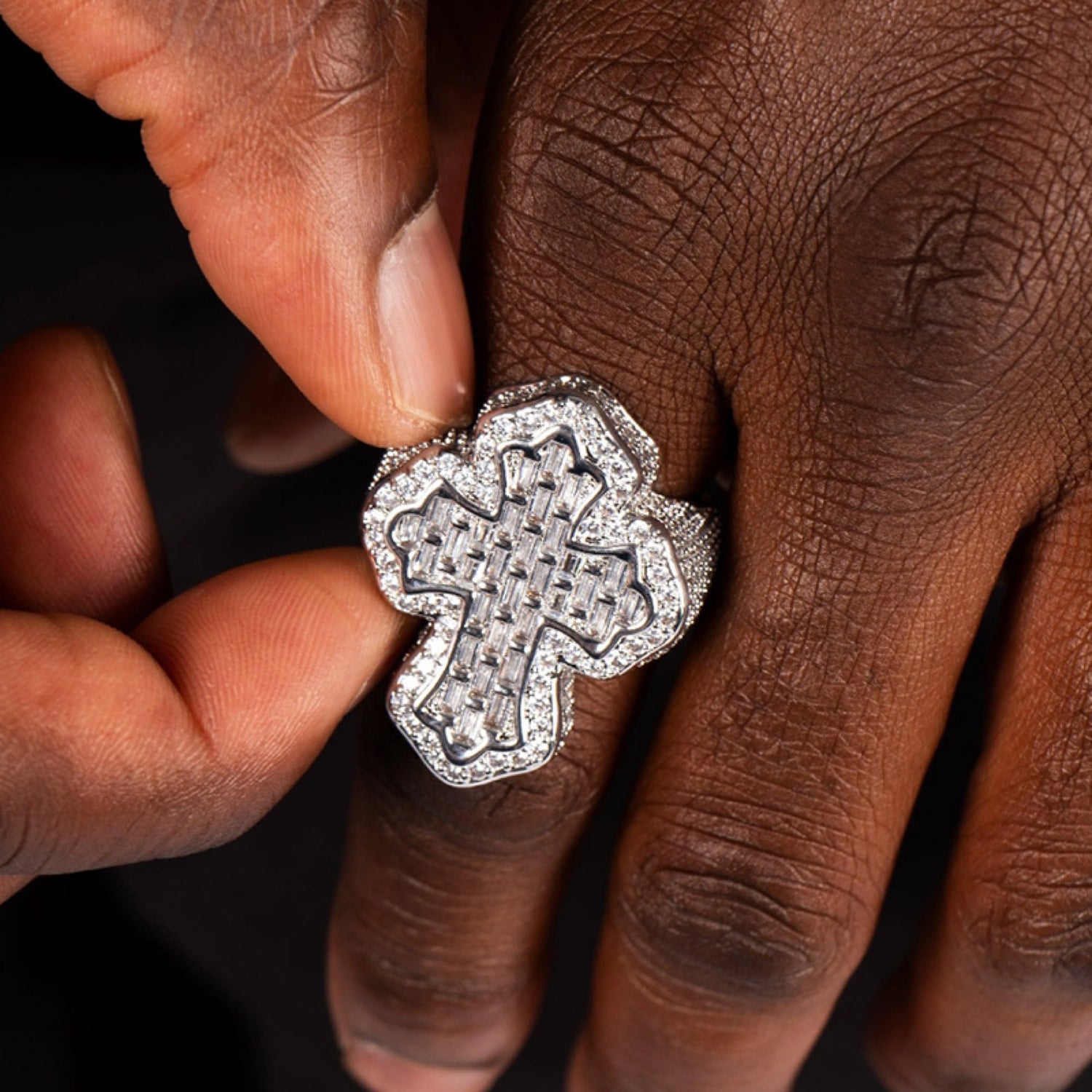 Silver iced baguette cross ring worn on a deep-brown hand