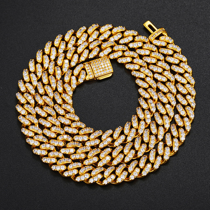 Gold-tone single-row moissanite Cuban chain coiled on black fabric with an open clasp