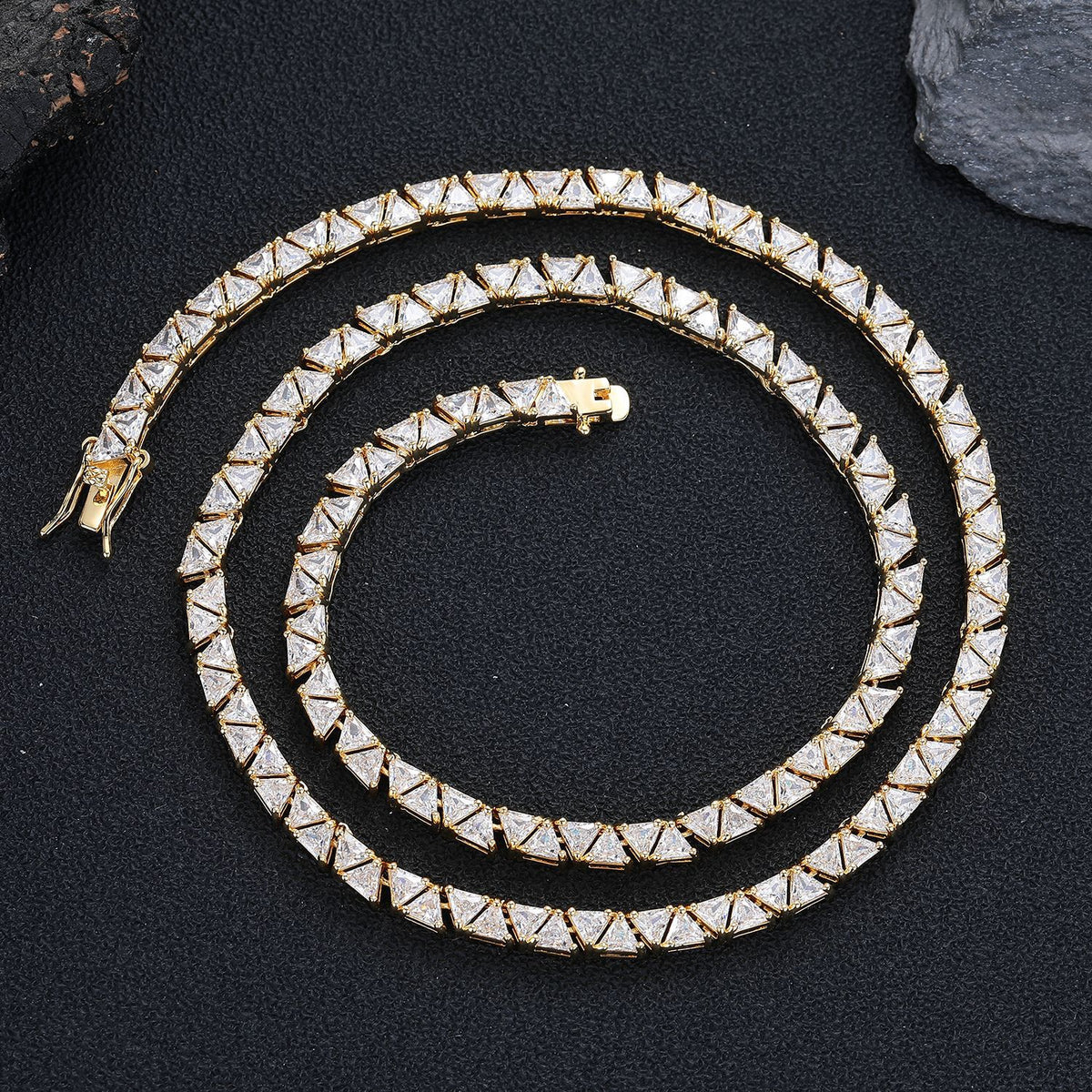 Gold-tone triangle tennis chain coiled on black fabric