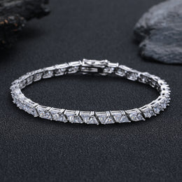 Silver-tone triangle tennis bracelet resting on black fabric beside rocks