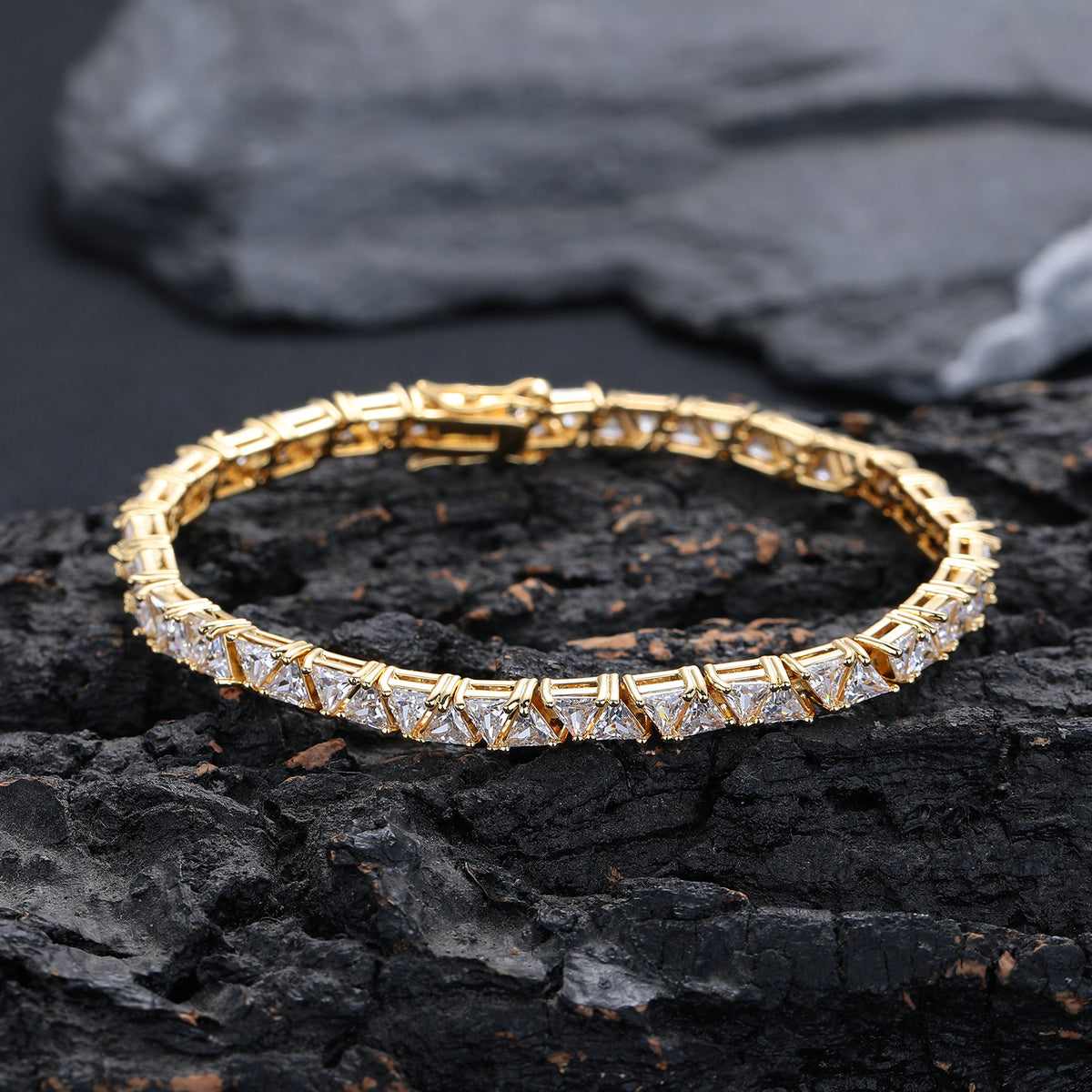 Gold-tone triangle tennis bracelet resting on a dark rock