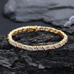 Gold-tone triangle tennis bracelet resting on a dark rock
