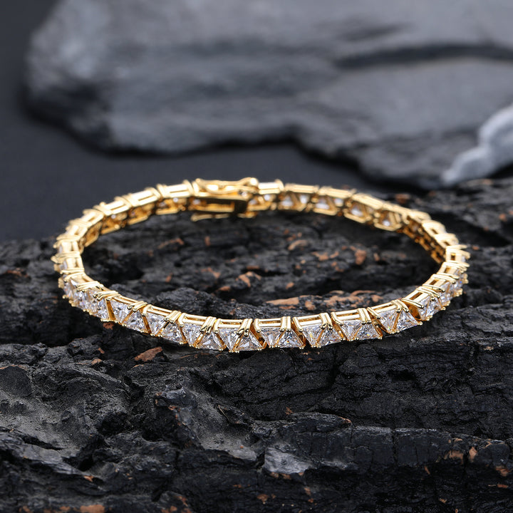 Gold-tone triangle tennis bracelet resting on a dark rock