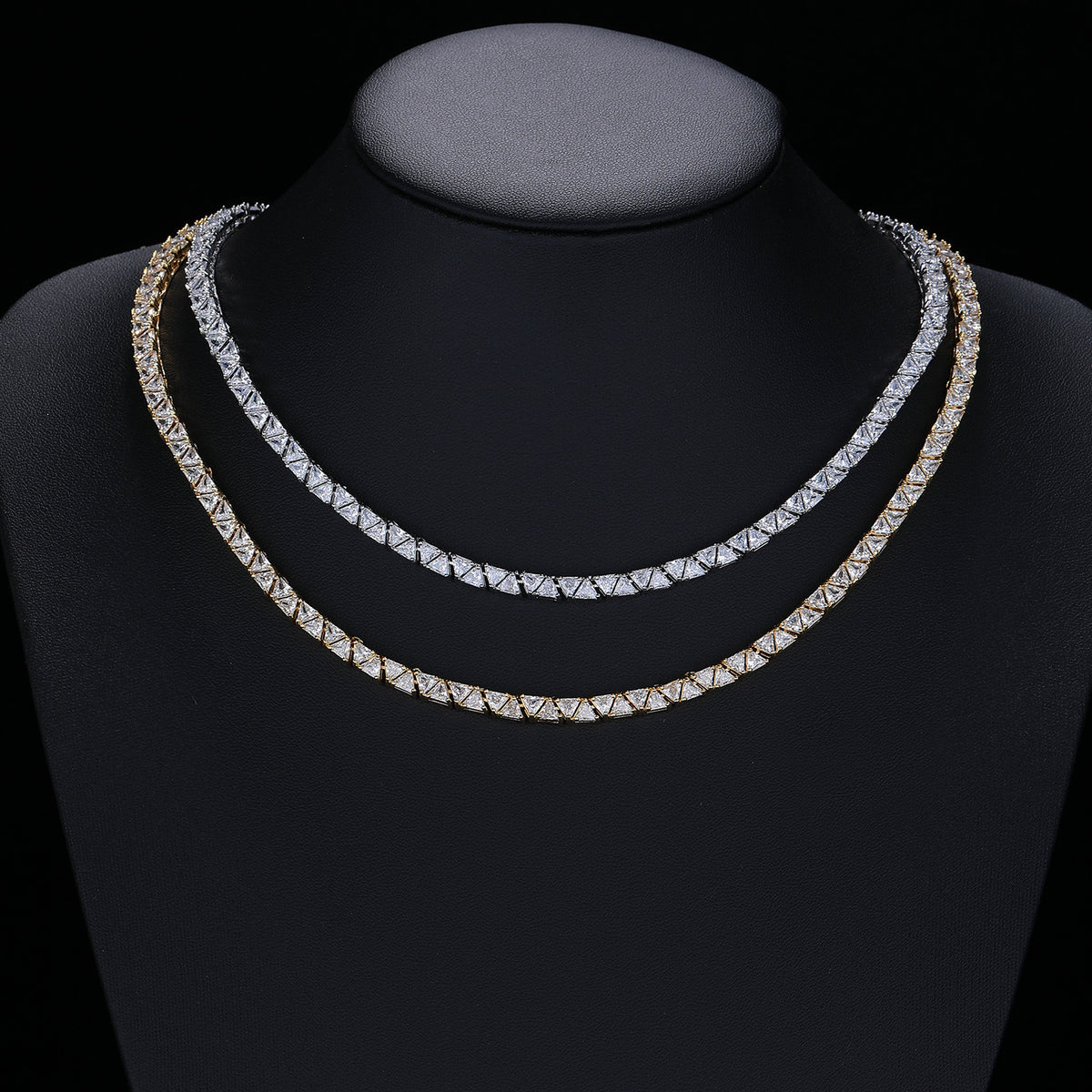 Silver- and gold-tone triangle tennis necklaces displayed on a black jewelry bust
