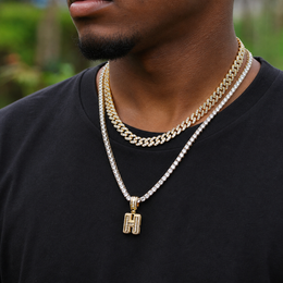 Gold iced baguette capital H initial pendant worn by a brown-skinned model