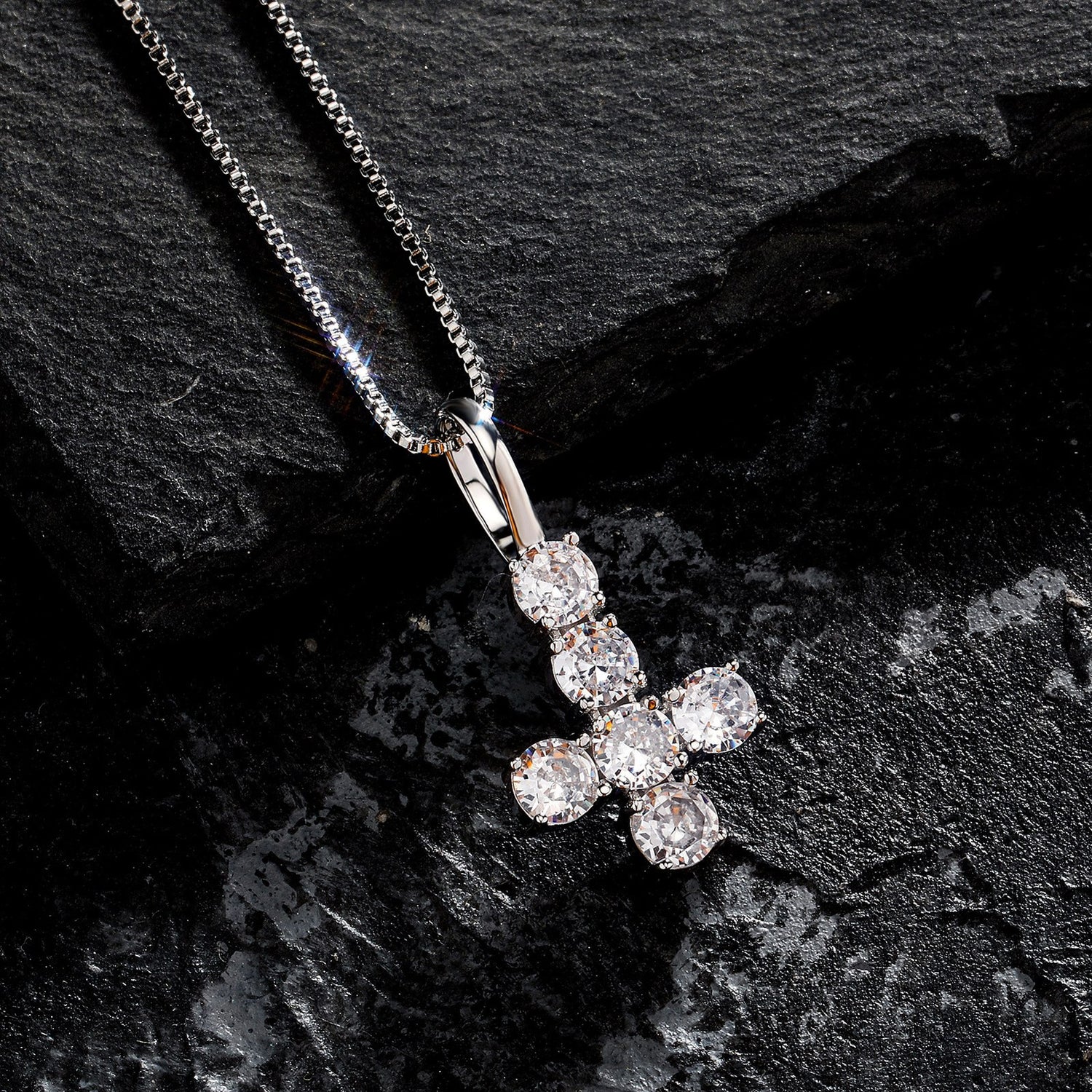 Silver iced inverted cross pendant displayed on black stone