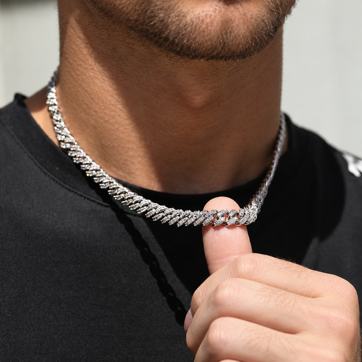 Adult model gently lifting a silver-tone moissanite Cuban chain with a thumb