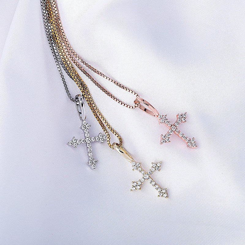 Three ornate cross pendant colors arranged on white fabric