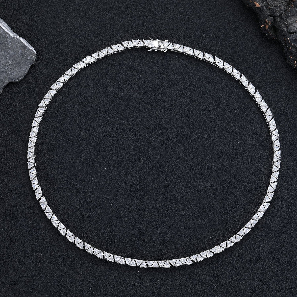Silver-tone triangle tennis chain arranged in a circle on black fabric
