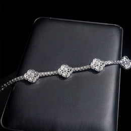 Reverse of a silver-tone clover tennis bracelet showing open back settings on a black display