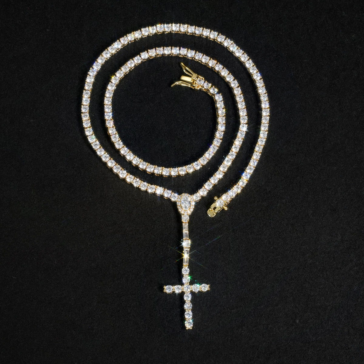 Gold-tone slender cross drop tennis necklace coiled on a black surface