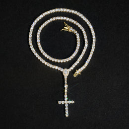 Gold-tone slender cross drop tennis necklace coiled on a black surface
