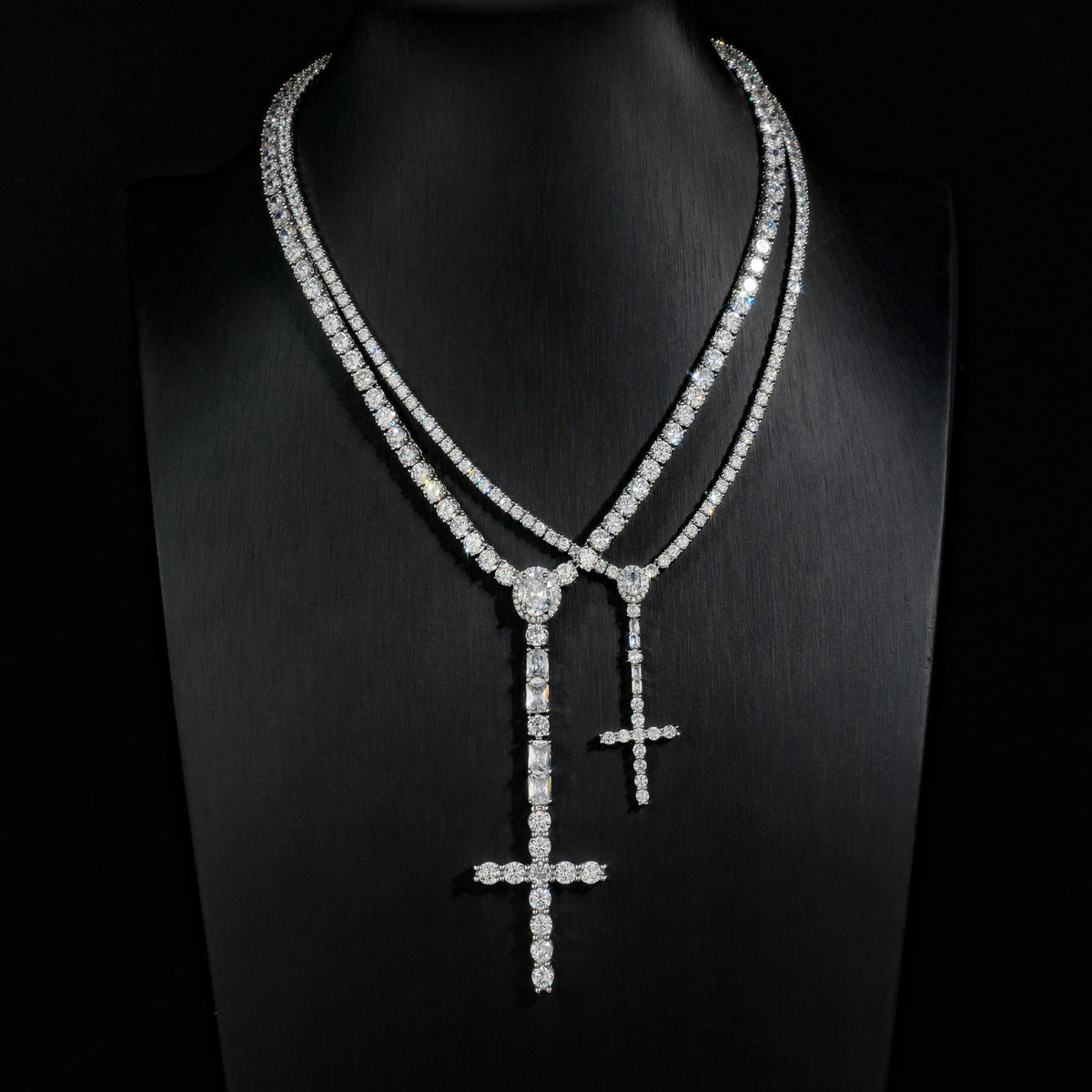 Comparison of slender and wider silver-tone cross drop tennis necklaces on a black display bust