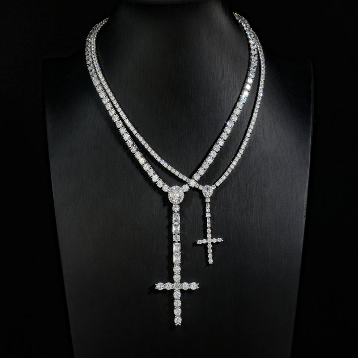 Comparison of slender and wider silver-tone cross drop tennis necklaces on a black display bust