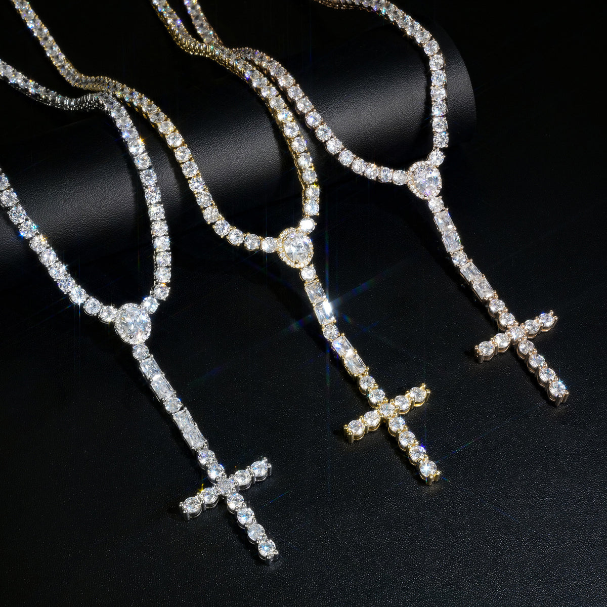 Silver, Gold and Rose Gold cross drop tennis necklaces draped over a black display roll