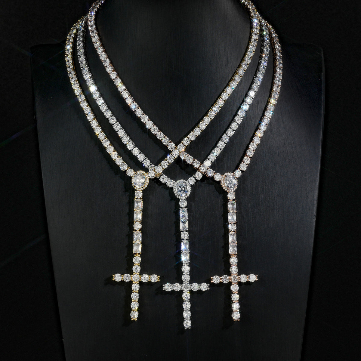 Three wider cross drop tennis necklaces in different finishes on a black display bust