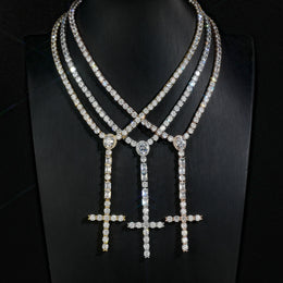 Three wider cross drop tennis necklaces in different finishes on a black display bust
