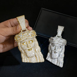 Gold-tone crowned Jesus pendant held beside a silver-tone pendant in a black box
