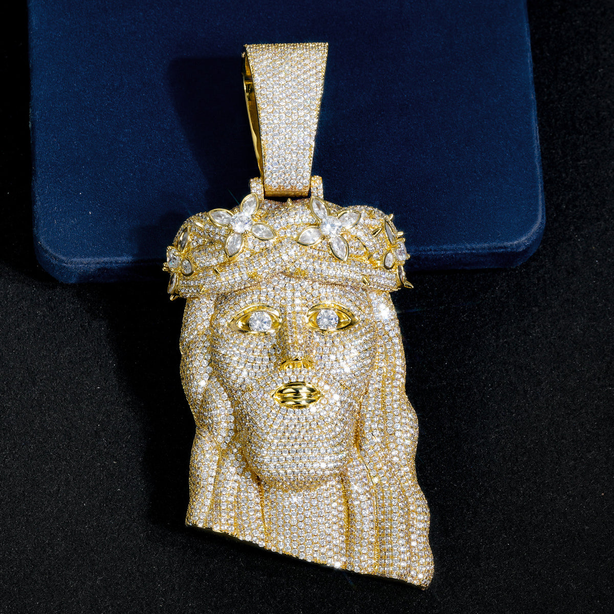 Close-up of a gold-tone crowned Jesus pendant against dark blue velvet