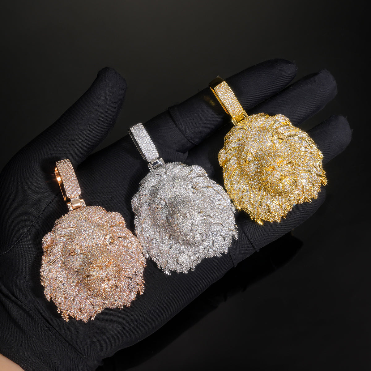 Three lion head pendants held in black-gloved hands