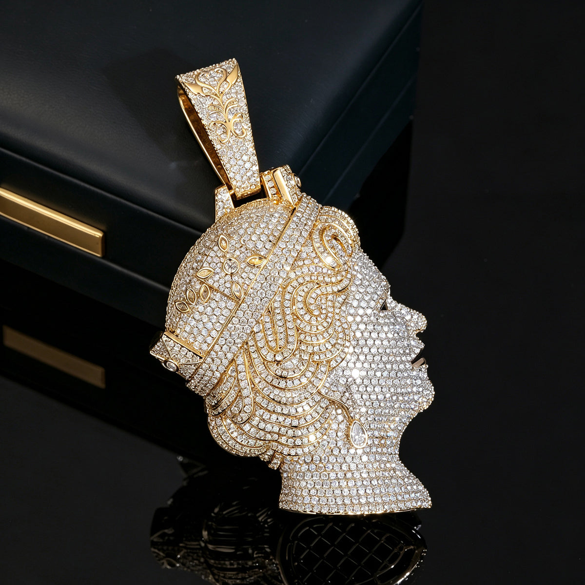 Gold-tone iced queen portrait pendant standing on a black reflective surface