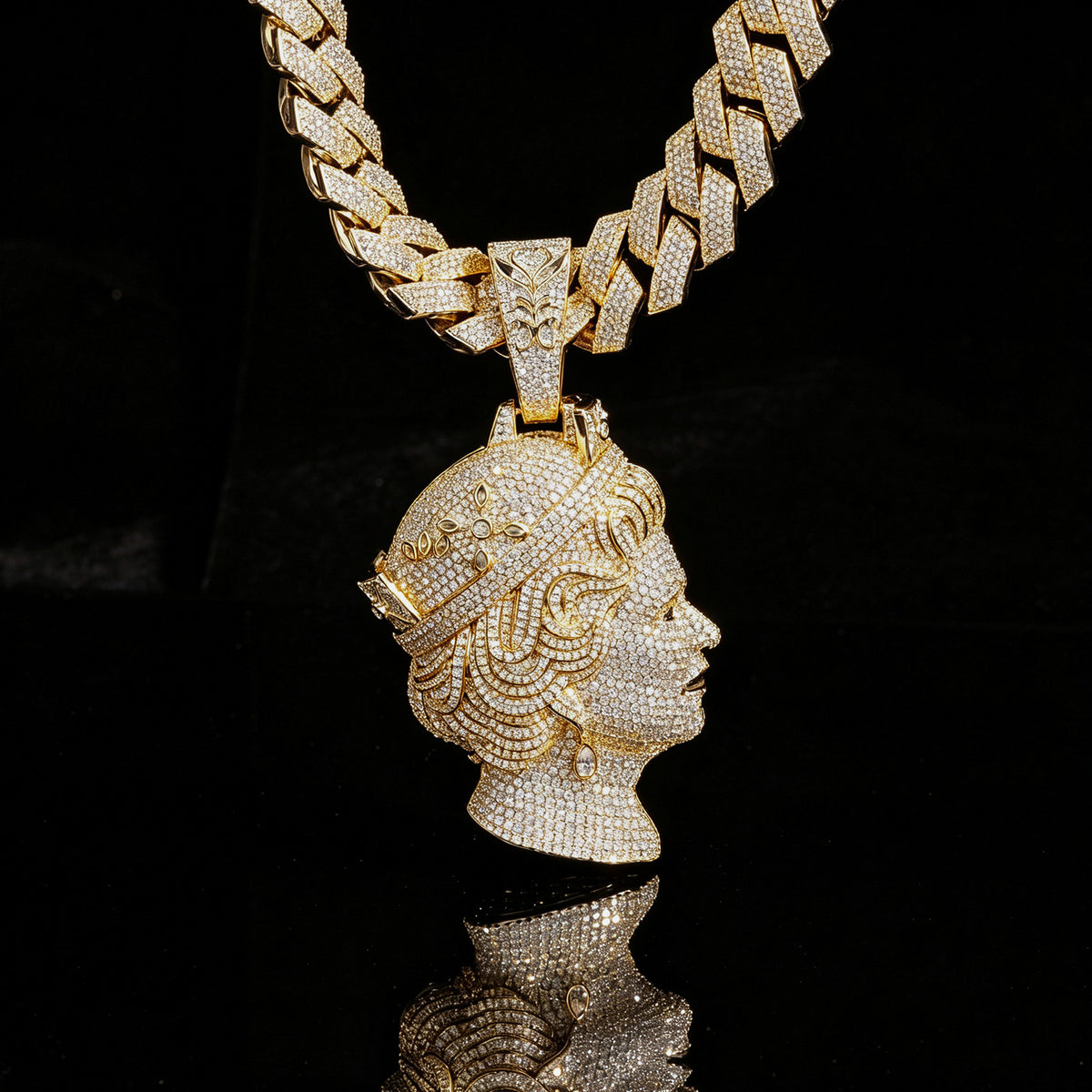 Gold-tone iced queen portrait pendant with its ornate bail against a black backdrop