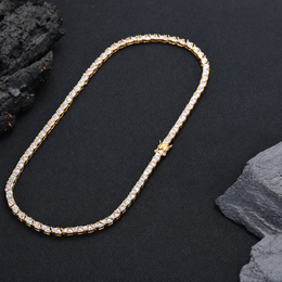 Gold-tone triangle tennis necklace laid in a long loop beside dark rocks