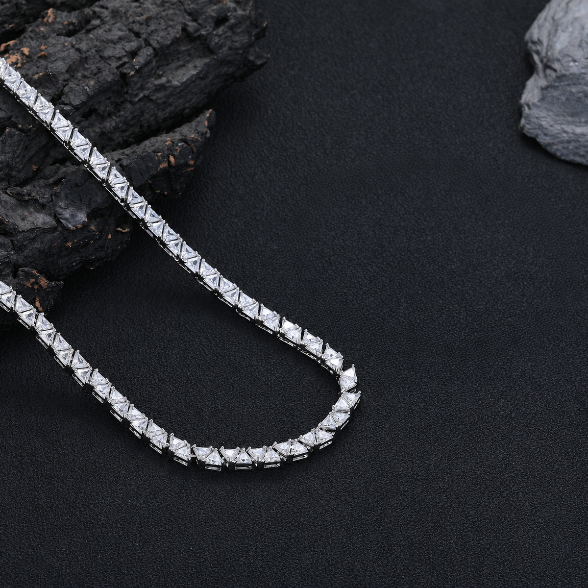 Silver-tone triangle tennis necklace curving across black fabric beside rocks