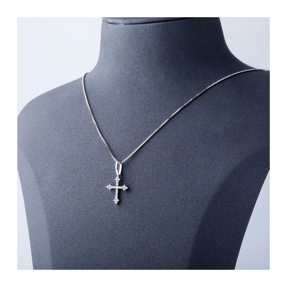 Silver iced ornate cross pendant displayed on a black bust