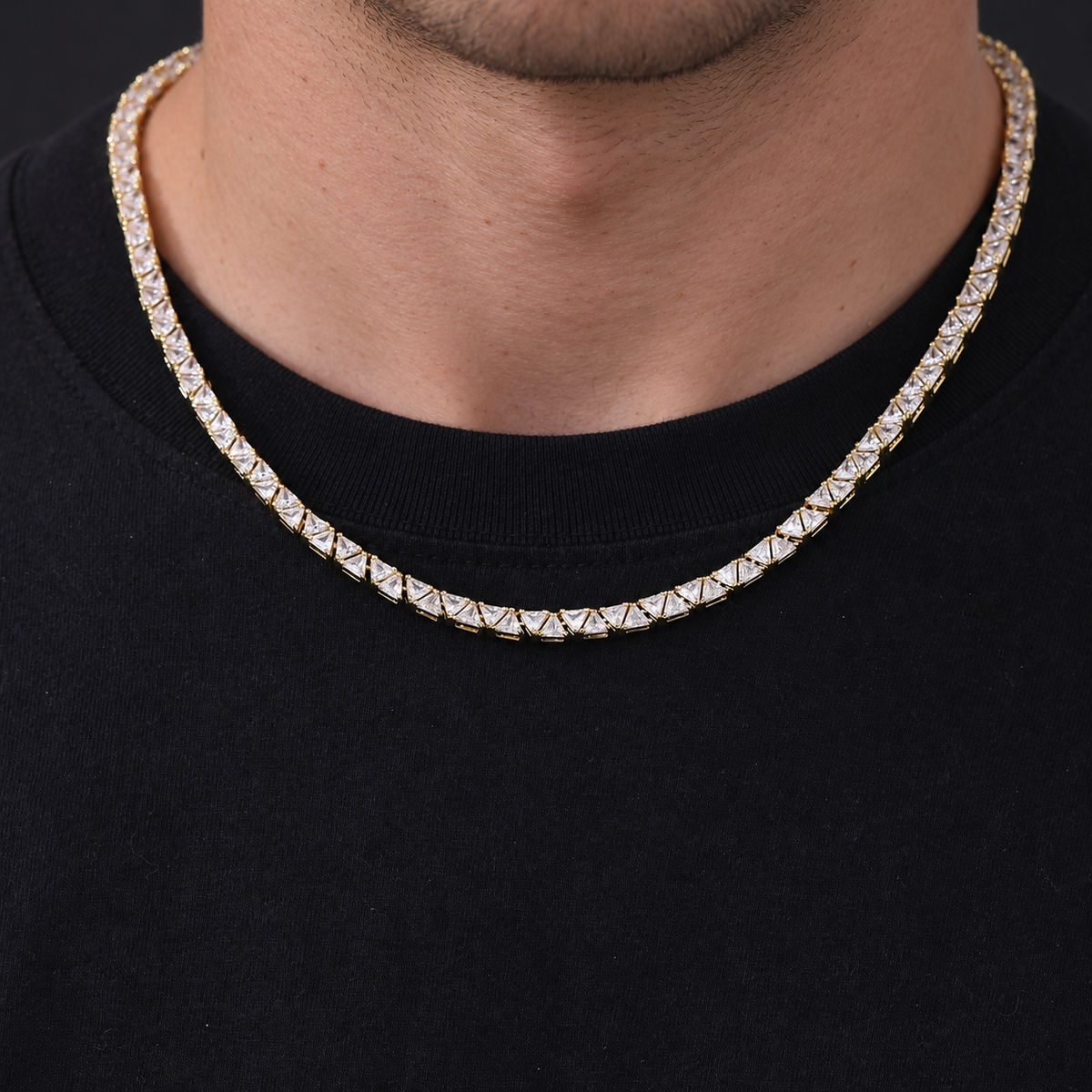 Adult model wearing a gold-tone triangle tennis necklace over a black crew-neck shirt