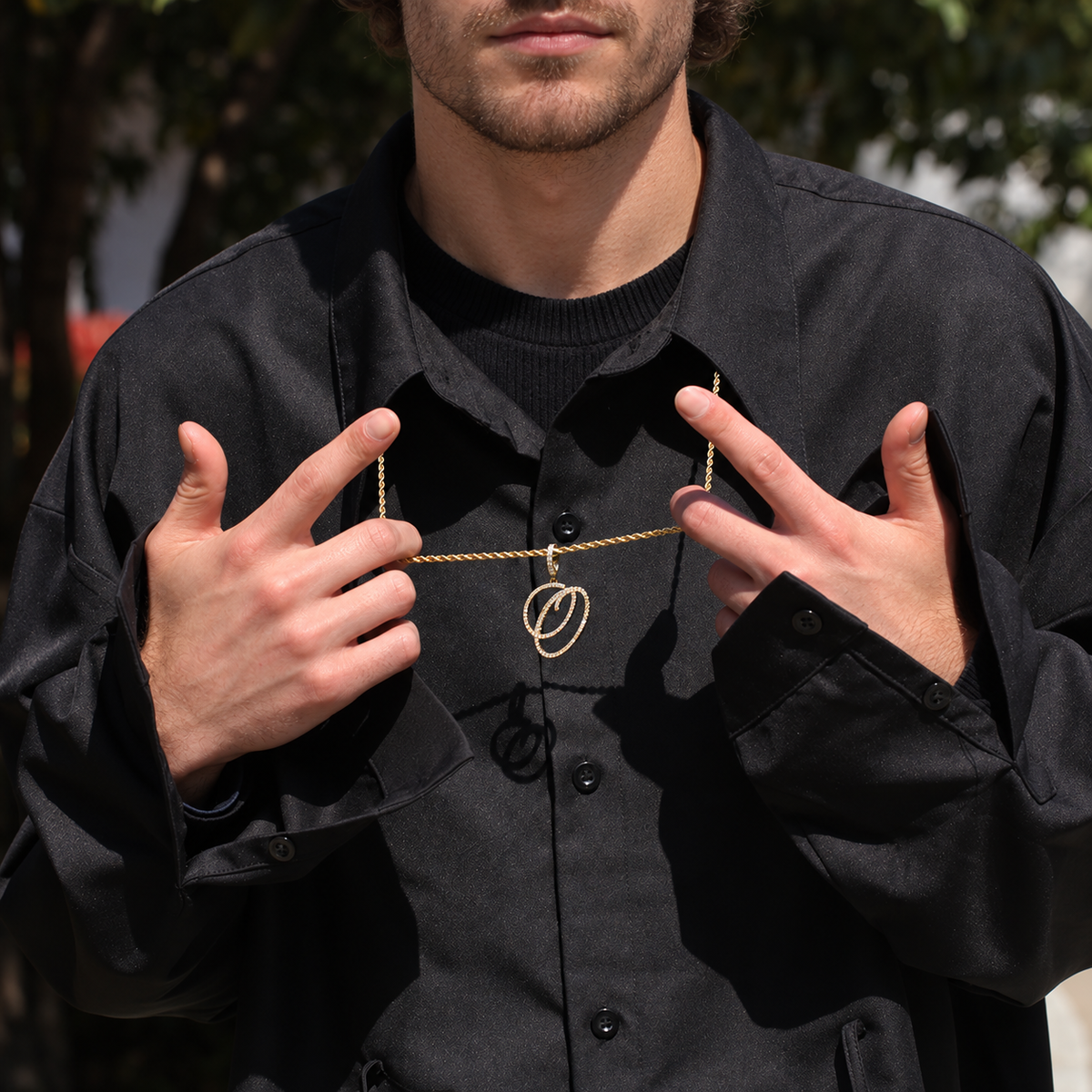 Model holding a gold-tone cubic zirconia script letter O pendant outdoors