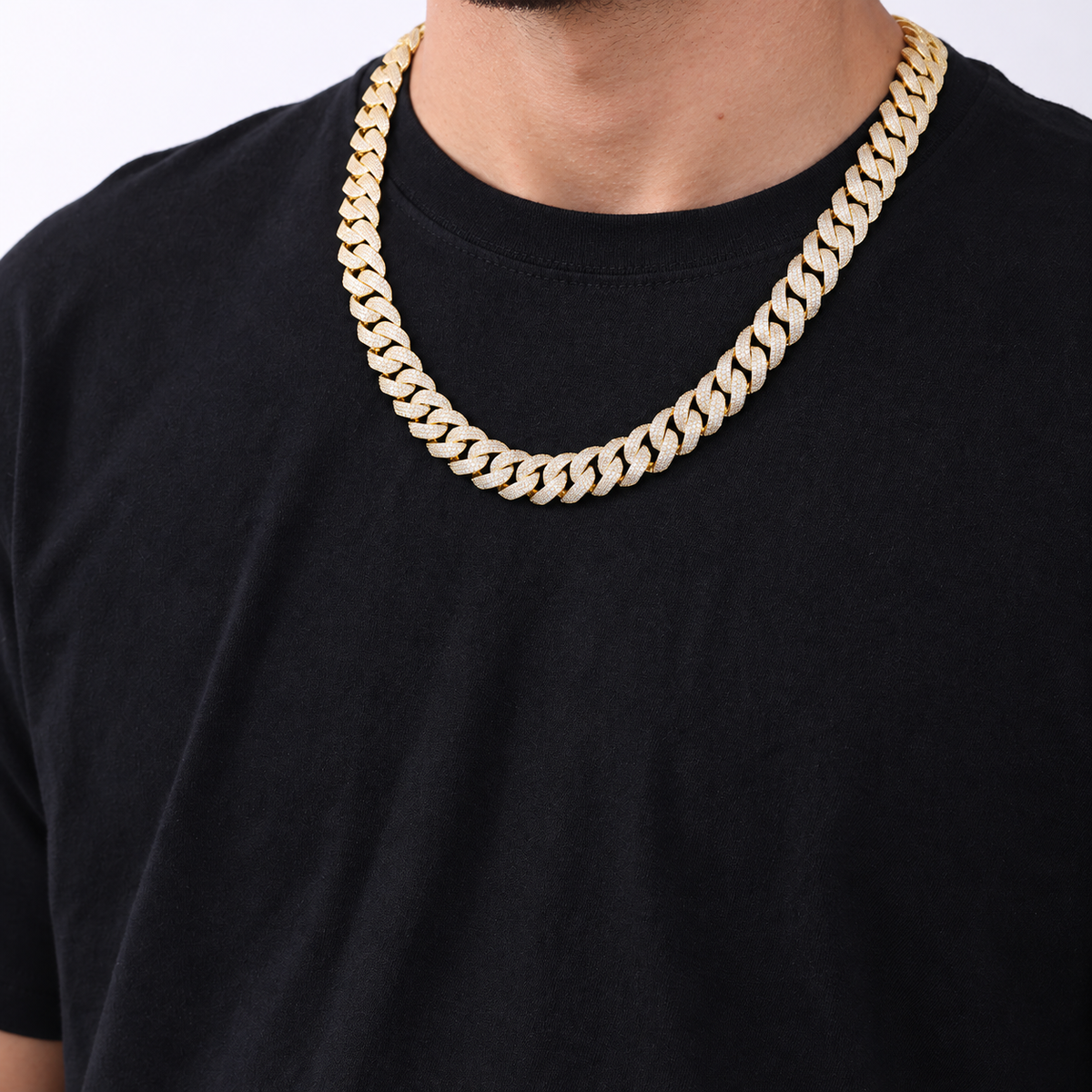Adult model wearing a gold-tone pavé Cuban chain over a black crew-neck shirt