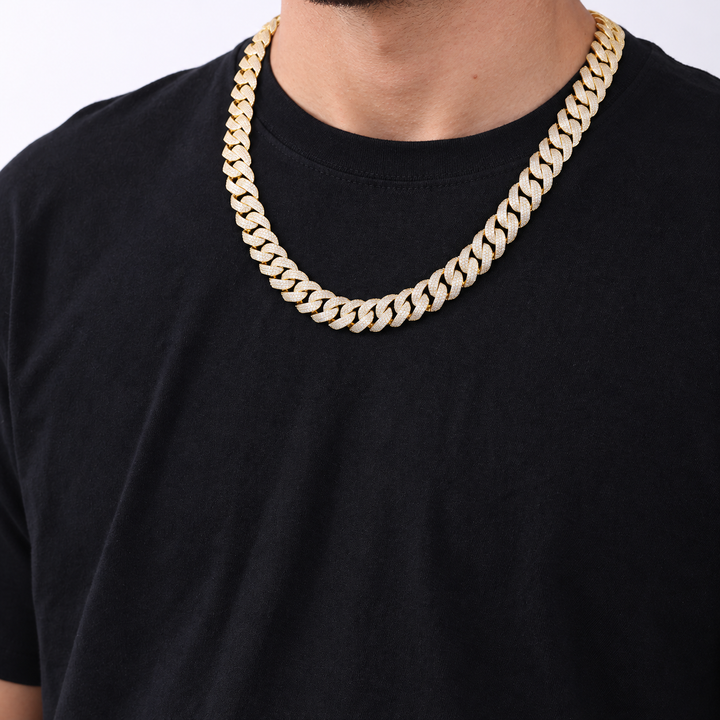 Adult model wearing a gold-tone pavé Cuban chain over a black crew-neck shirt
