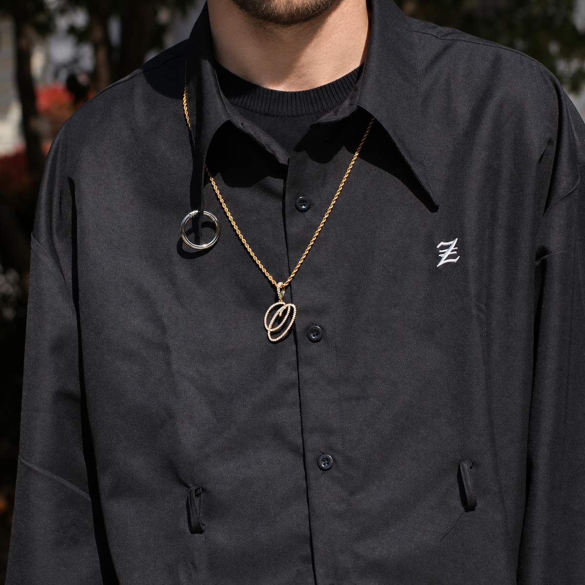 Model wearing a gold-tone cubic zirconia script letter O pendant outdoors