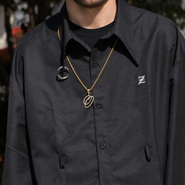 Model wearing a gold-tone cubic zirconia script letter O pendant outdoors