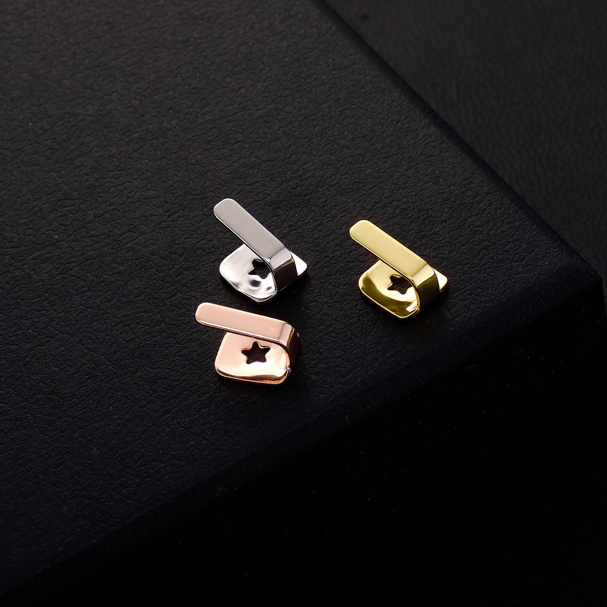 Gold, Silver and Rose Gold bar tooth caps showing star-shaped openings on black textured fabric