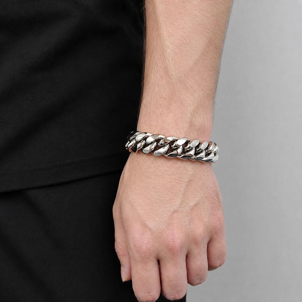 Silver-tone wide Cuban link bracelet worn on the wrist beside black clothing