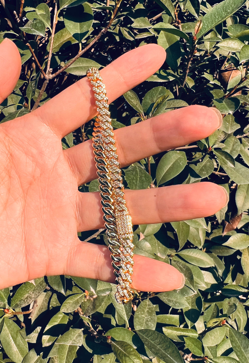 Gold iced out Cuban link bracelet with diamonds held in hand outdoors - Miles Jewellery