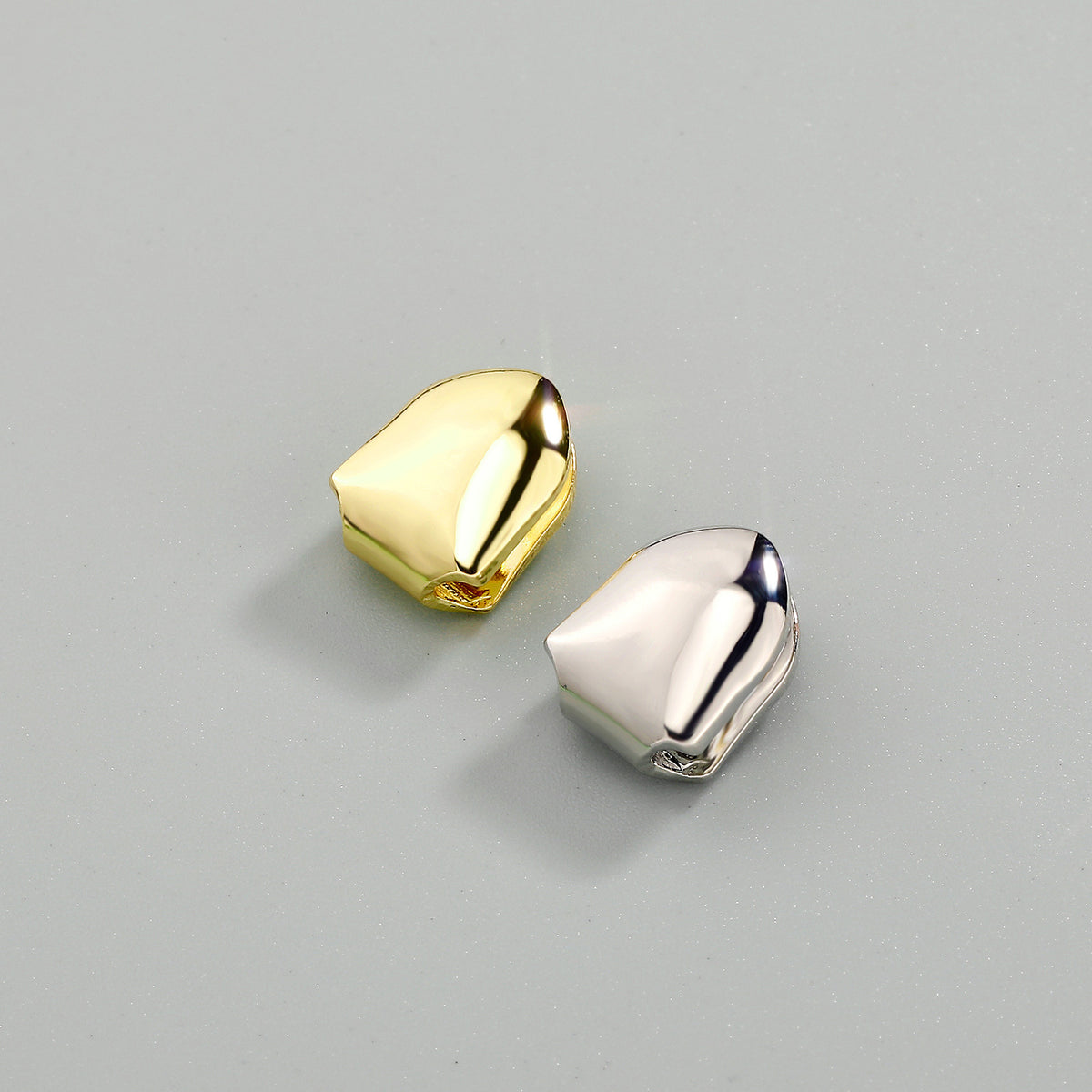 Gold-tone and silver-tone single tooth grills displayed together on a grey surface