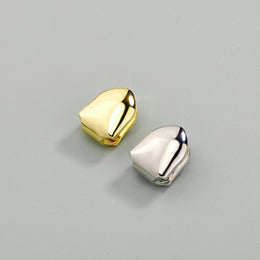 Gold-tone and silver-tone single tooth grills displayed together on a grey surface