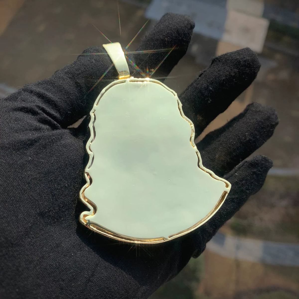 Smooth gold-tone back of a Jesus portrait pendant held against a black glove