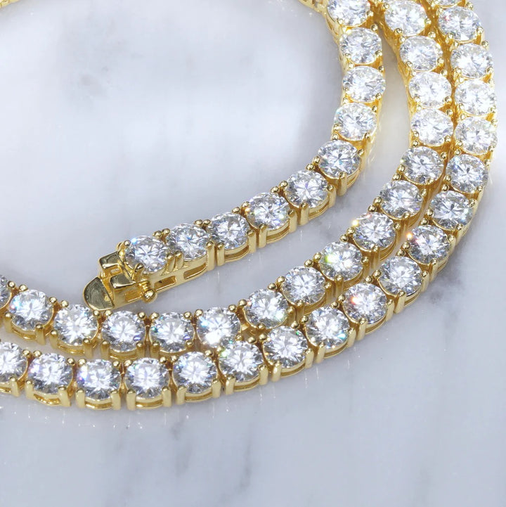 Gold-tone CZ tennis chains with round stones on white marble
