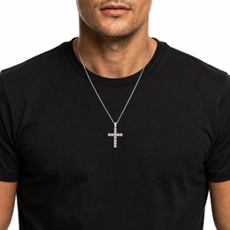 A man wearing a silver cross pendant necklace with clear stones, shown against a plain white background.