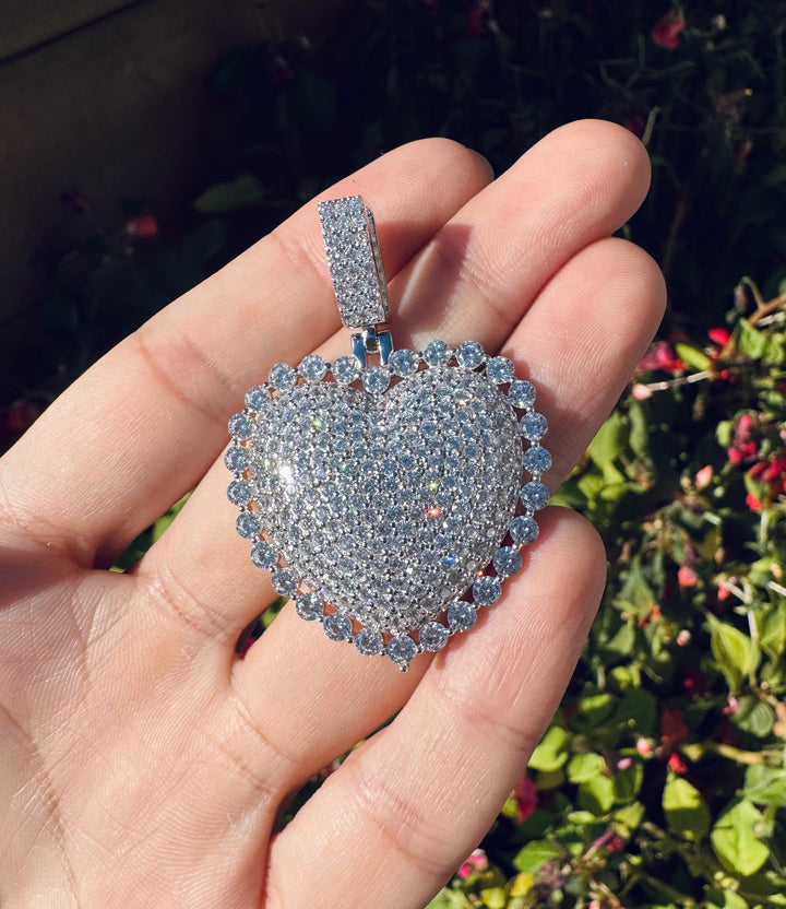 Silver-tone heart pendant covered in clear stones held in a hand