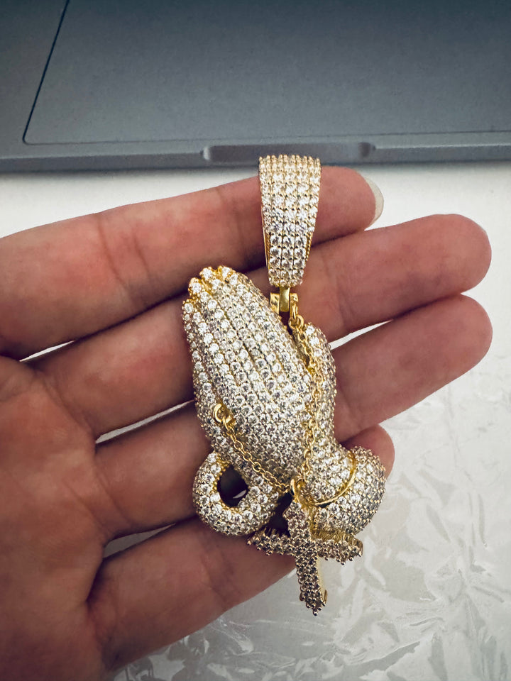 Gold-tone stone-set praying hands pendant with a hanging cross held in a hand