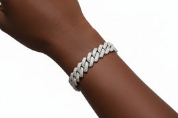 A close-up of a silver-toned braided chain bracelet with pavé-set clear stones worn on a person's wrist against a black shirt background.